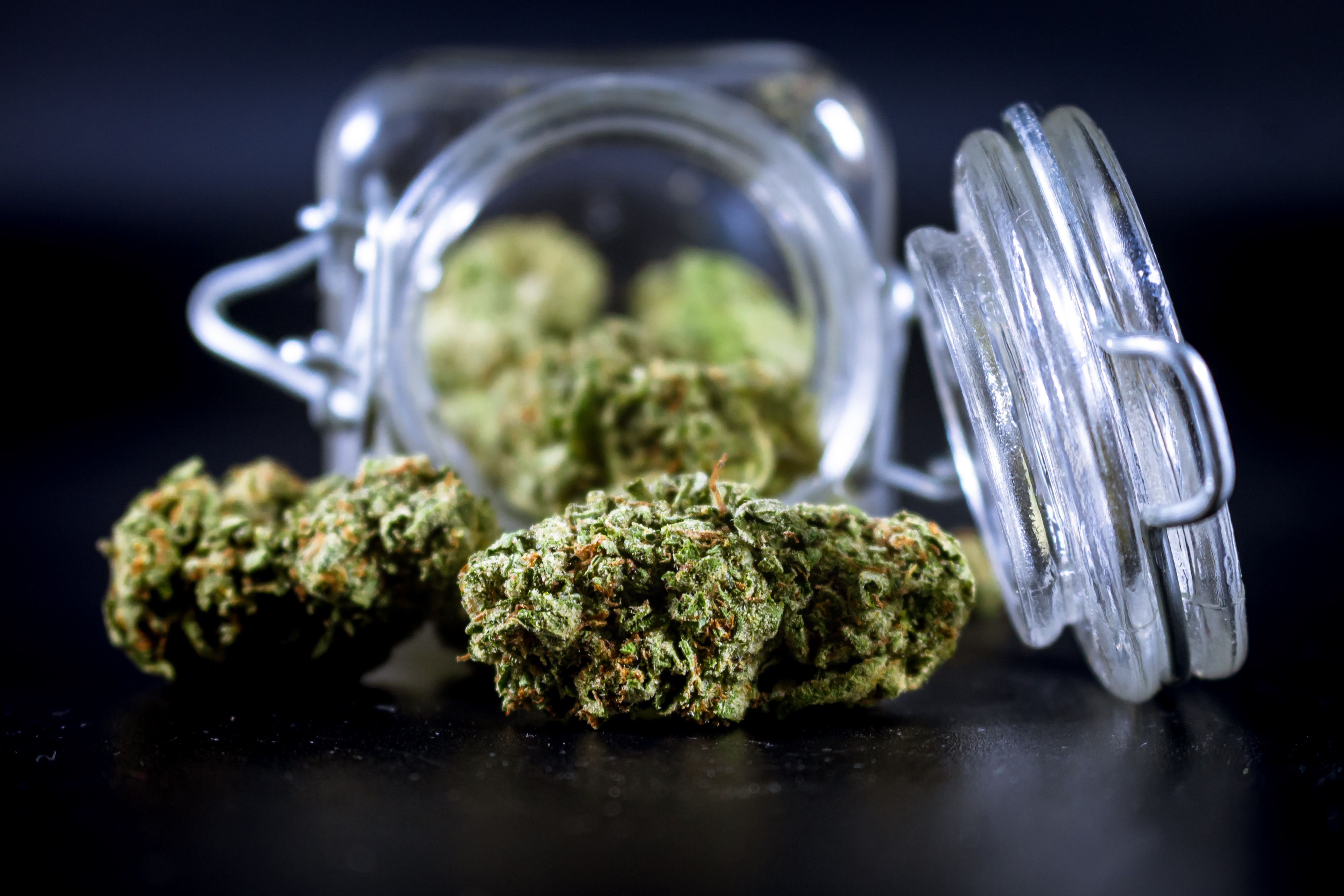 High-quality cannabis buds partially spilling from an open glass jar
