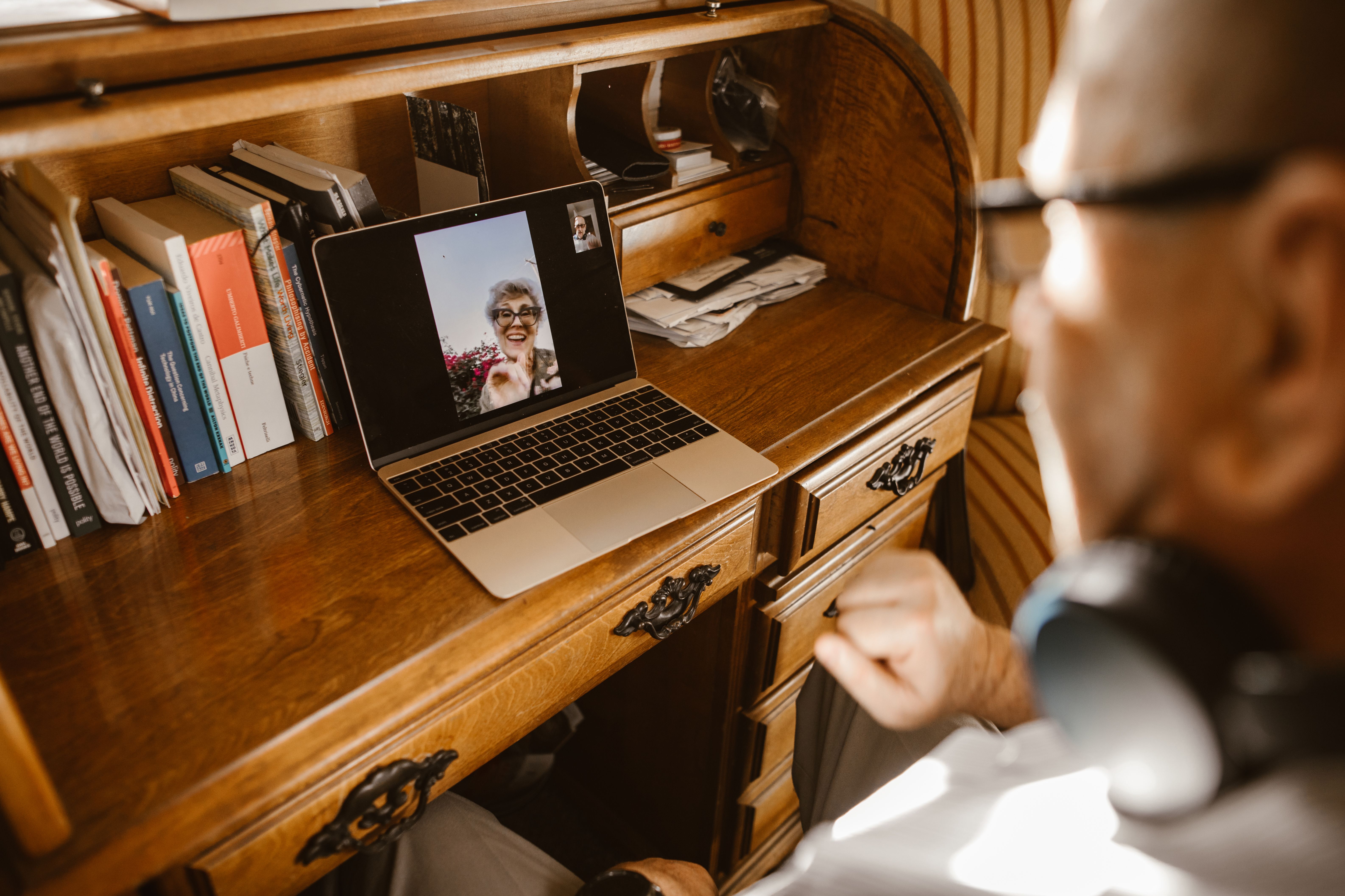 An elderly man video calling a woman on a laptop, illustrating connection across distance and generations.