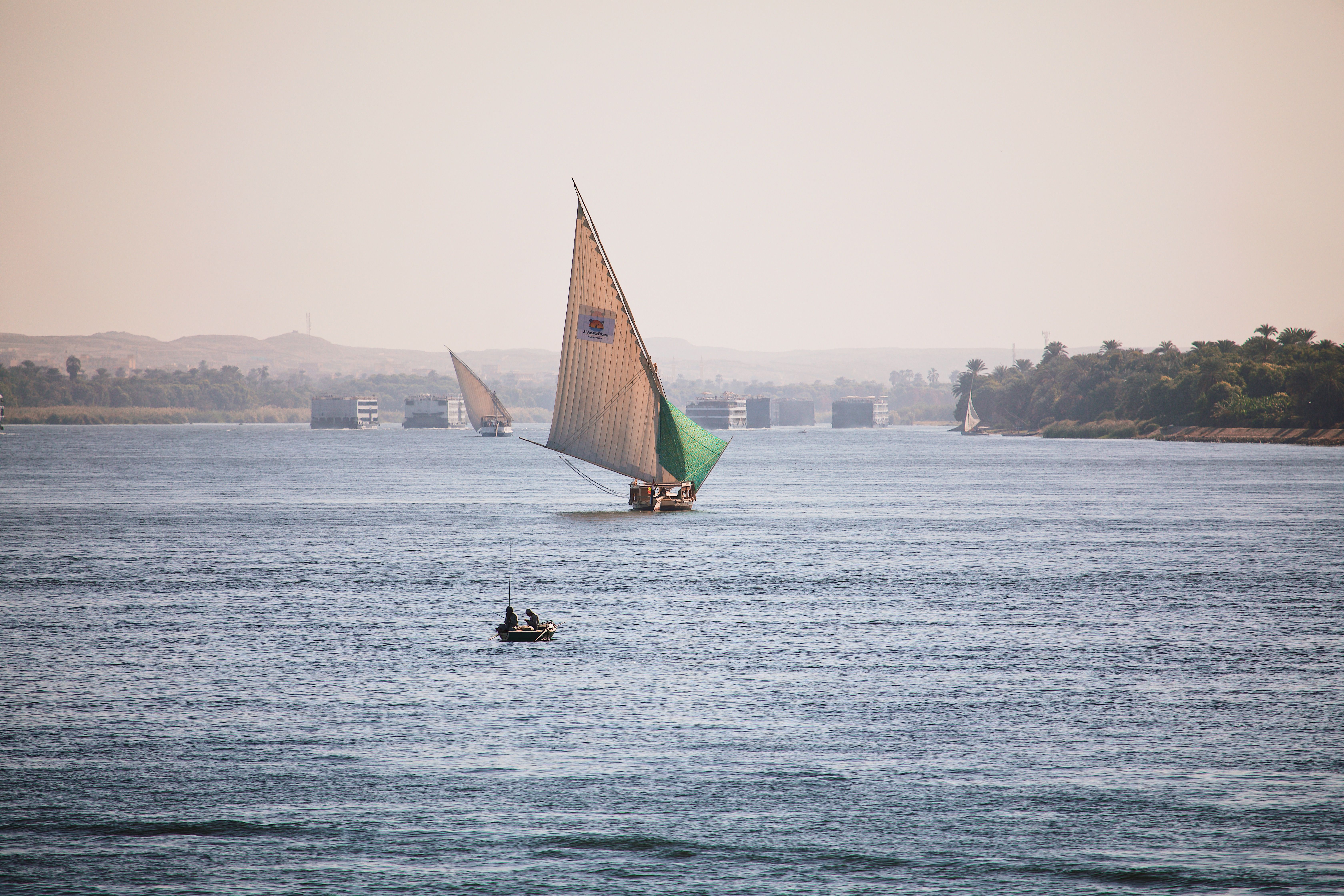 A traditional felucca sailing on the Nile River in Luxor, Egypt, under a clear blue sky.